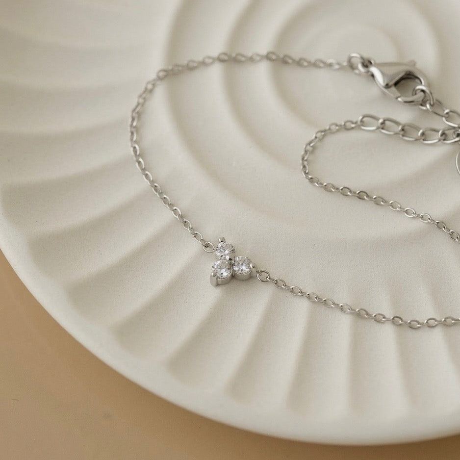 Dainty silver white gold chain bracelet with a sparkling crystal charm displayed on an aesthetic white ceramic tray, luxury minimalist silver jewelry by Lumire.