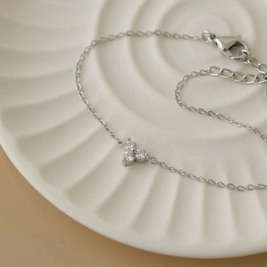 Dainty silver white gold chain bracelet with a sparkling crystal charm displayed on an aesthetic white ceramic tray, luxury minimalist silver jewelry by Lumire.
